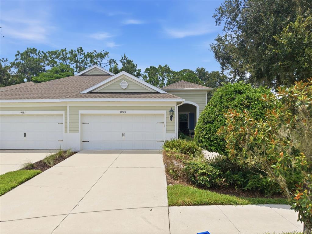 A duplex house with light green siding, two white garage doors, and a concrete driveway — 13584 CIRCA CROSSING DRIVE, LITHIA, FL