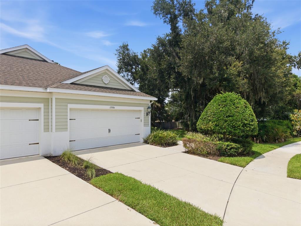 A light green house exterior features a two-car garage and a concrete driveway — 13584 CIRCA CROSSING DRIVE, LITHIA, FL