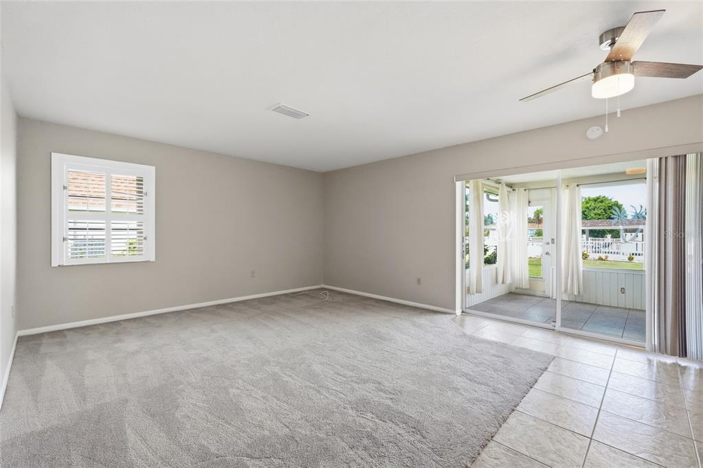A living room features gray carpet, beige walls, a ceiling fan, and sliding glass patio doors — 7206 10TH AVENUE W, BRADENTON, FL