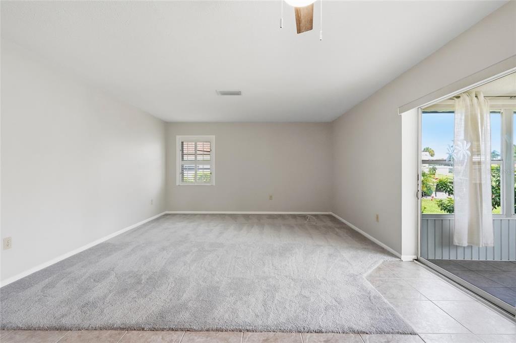 A living room with gray carpet, light walls, a ceiling fan, and sliding glass doors — 7206 10TH AVENUE W, BRADENTON, FL