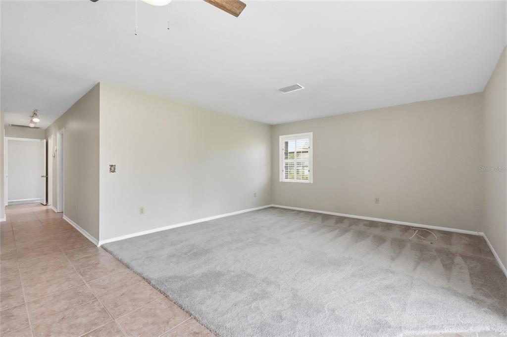 A spacious room features light-colored walls, gray carpeting, a ceiling fan, and a single window — 7206 10TH AVENUE W, BRADENTON, FL