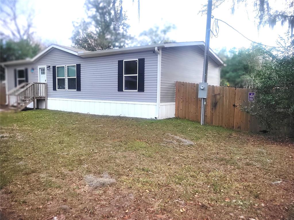 A single-story manufactured home with grey siding and a wooden fence in the yard — 2829 N LAKEFRONT DRIVE, HERNANDO, FL