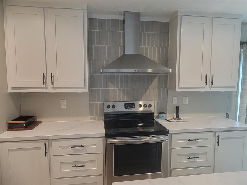 A kitchen features white cabinets, a stainless steel range, a vent hood, and gray tile backsplash — 2829 N LAKEFRONT DRIVE, HERNANDO, FL