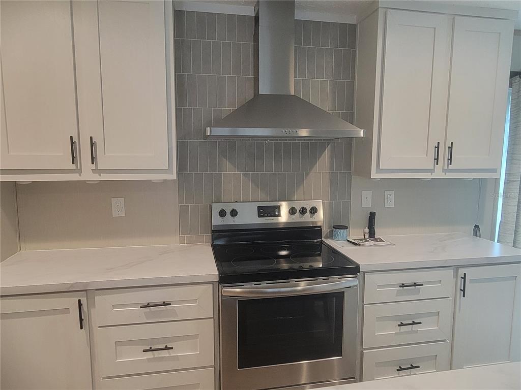 A kitchen features white cabinets, stainless steel appliances, and a gray vertical tile backsplash — 2829 N LAKEFRONT DRIVE, HERNANDO, FL