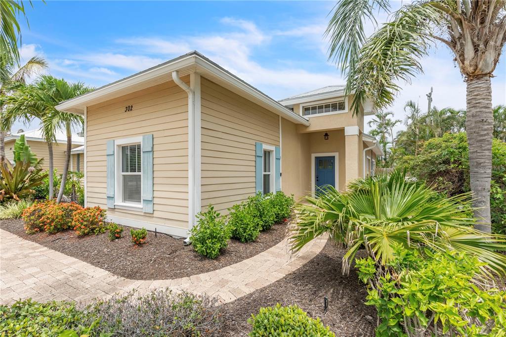 A tan, single-story house with blue shutters and a paved walkway surrounded by tropical landscaping — 302 67TH STREET, HOLMES BEACH, FL