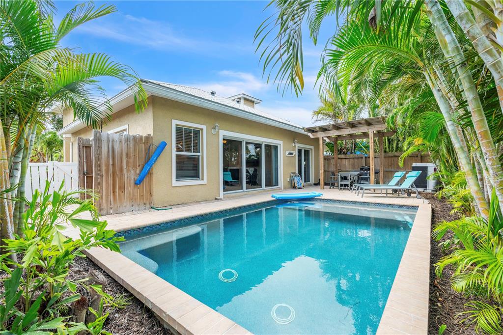 A backyard features a rectangular swimming pool, a patio with lounge chairs, and palm trees — 302 67TH STREET, HOLMES BEACH, FL