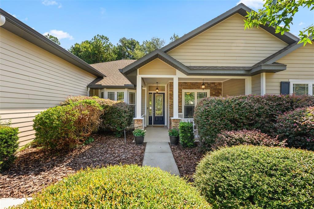 The exterior of a single-story house features beige siding, a stone facade, and landscaping — 7585 SW 79TH DRIVE, GAINESVILLE, FL