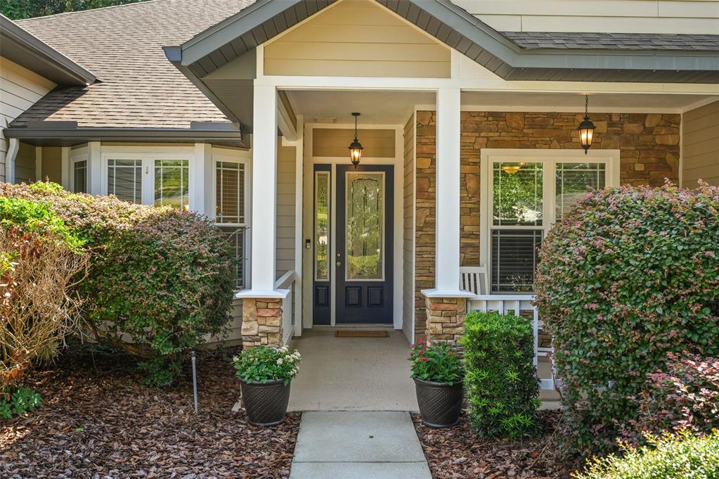 A front entrance with a dark blue door, stone accents, and two potted plants — 7585 SW 79TH DRIVE, GAINESVILLE, FL