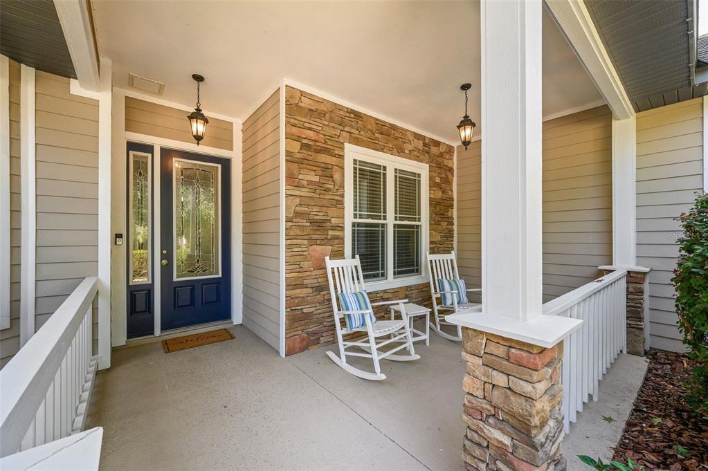 A covered front porch features a blue door, stone siding, and two white rocking chairs — 7585 SW 79TH DRIVE, GAINESVILLE, FL