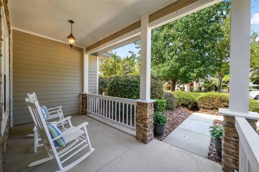 A covered front porch features two white rocking chairs, stone pillars, and a concrete walkway — 7585 SW 79TH DRIVE, GAINESVILLE, FL