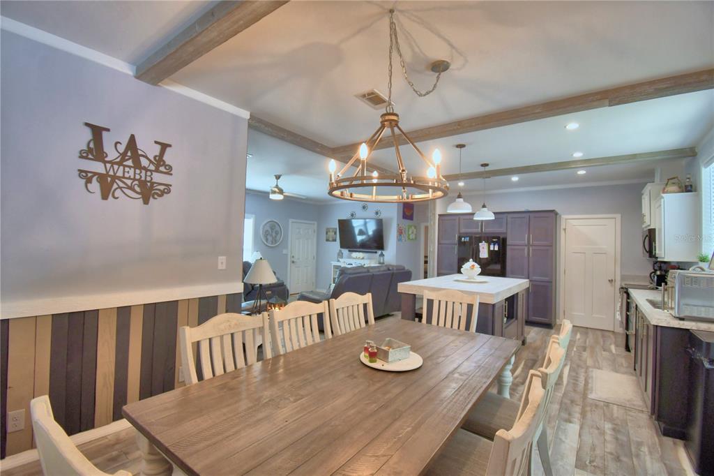 A dining area with a wooden table and chandelier opens into a kitchen and living room — 2497 US HIGHWAY 98 W, FROSTPROOF, FL