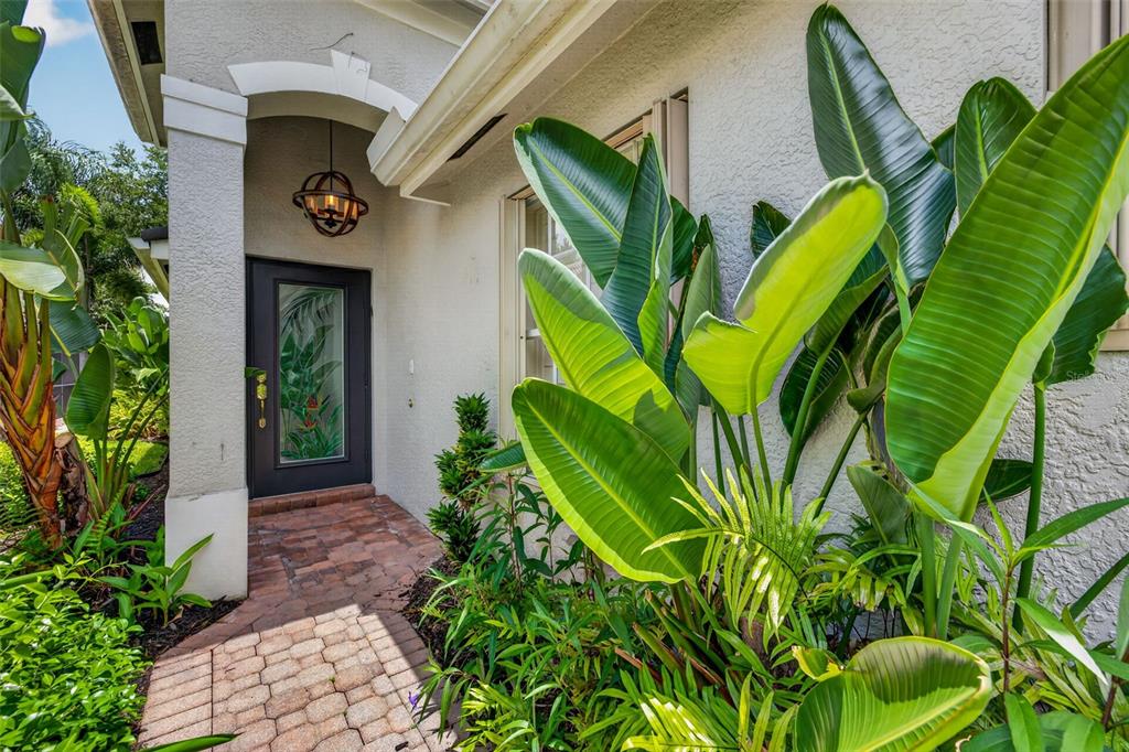 A paved walkway leads to a front door with a decorative glass insert and porch light — 1574 WINDAMERE LANE, NAPLES, FL