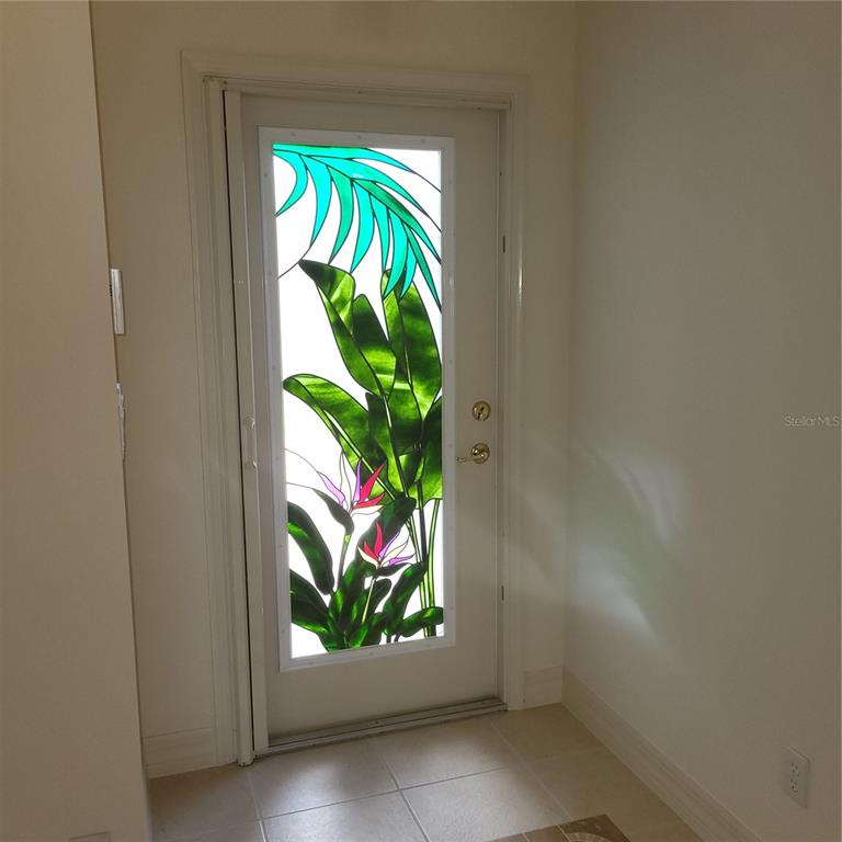 An interior view of a white door featuring a stained glass panel with tropical floral designs — 1574 WINDAMERE LANE, NAPLES, FL