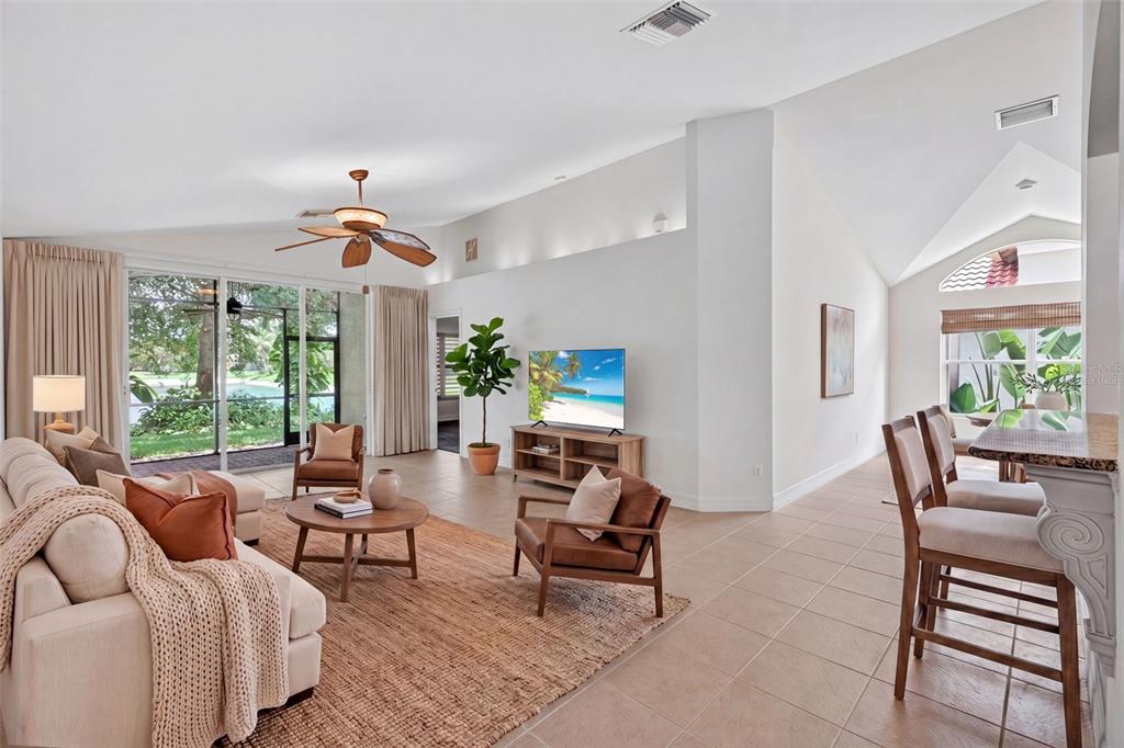 A bright living room features tile floors, a vaulted ceiling, and sliding doors to a patio — 1574 WINDAMERE LANE, NAPLES, FL