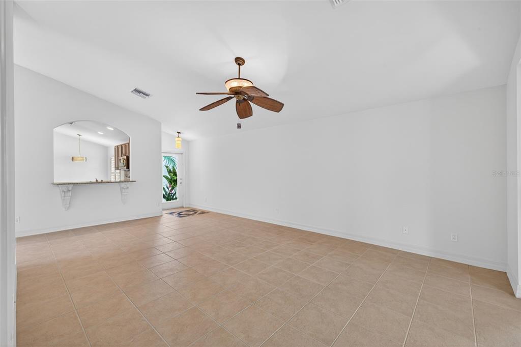 A bright, empty living room features beige tile flooring, white walls, and a ceiling fan — 1574 WINDAMERE LANE, NAPLES, FL