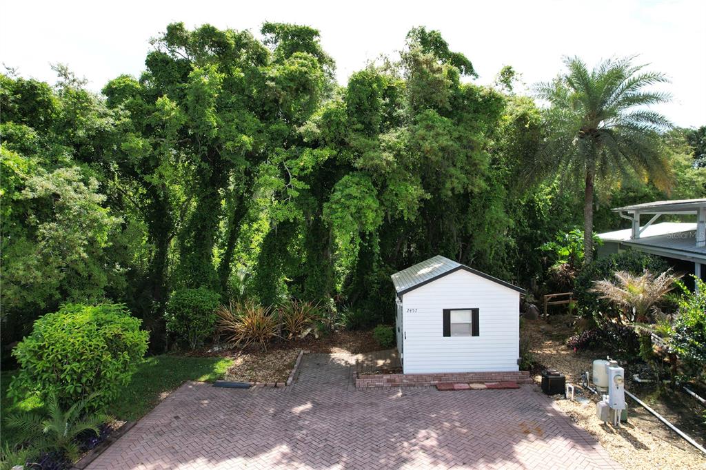 A small white shed sits on a brick-paved driveway in front of a dense forest — 2457 ST GEORGE DRIVE, DAVENPORT, FL