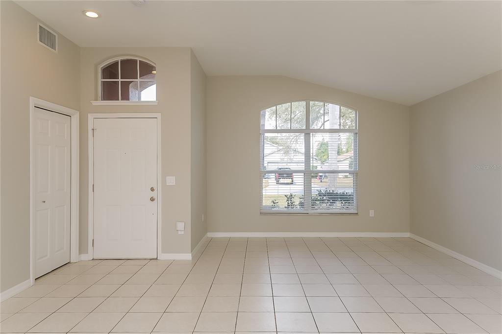 An empty room with beige walls, tile flooring, a front door, and a large arched window — 1723 WESTERLY DR, BRANDON, FL