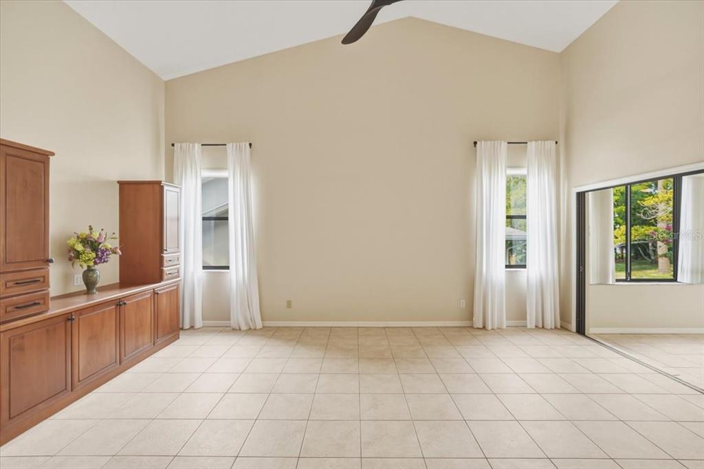 A living room with vaulted ceilings, tile flooring, built-in wooden cabinetry, and large windows — 58 BYRSONIMA CIRCLE, HOMOSASSA, FL