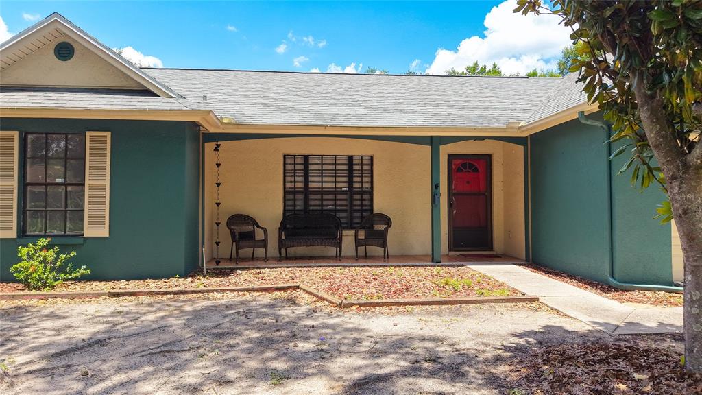 The exterior of a single-story house features a covered porch, dark green siding, and a red door — 1048 MALLETWOOD DRIVE, BRANDON, FL