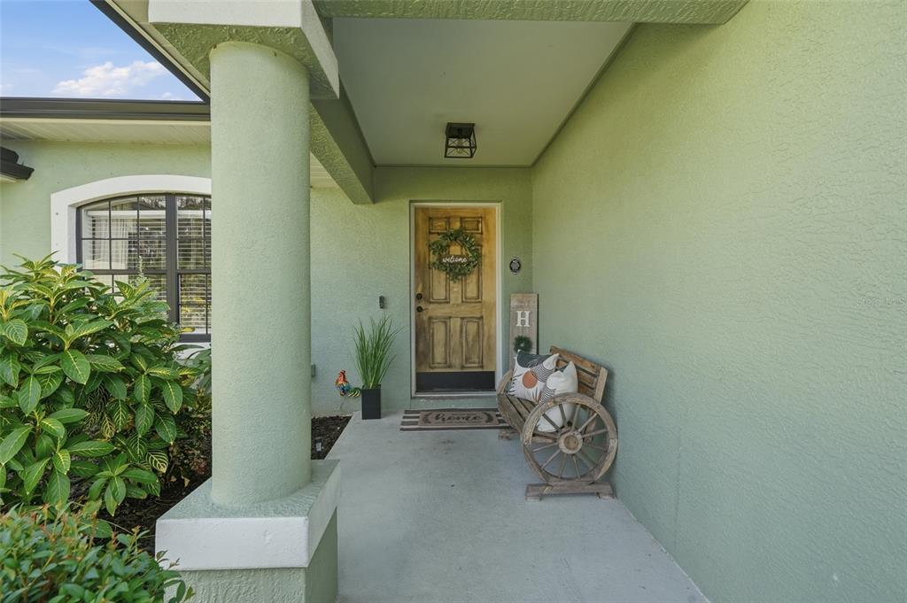 A covered front porch with a wooden door, a wagon wheel bench, and green stucco walls — 2244 PENGUIN LANE, NORTH PORT, FL