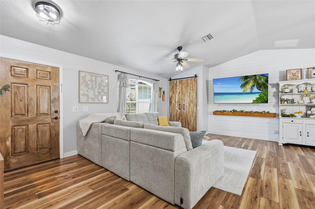 A living room features a sectional sofa, wood-look flooring, a wall-mounted television, and barn doors — 2244 PENGUIN LANE, NORTH PORT, FL