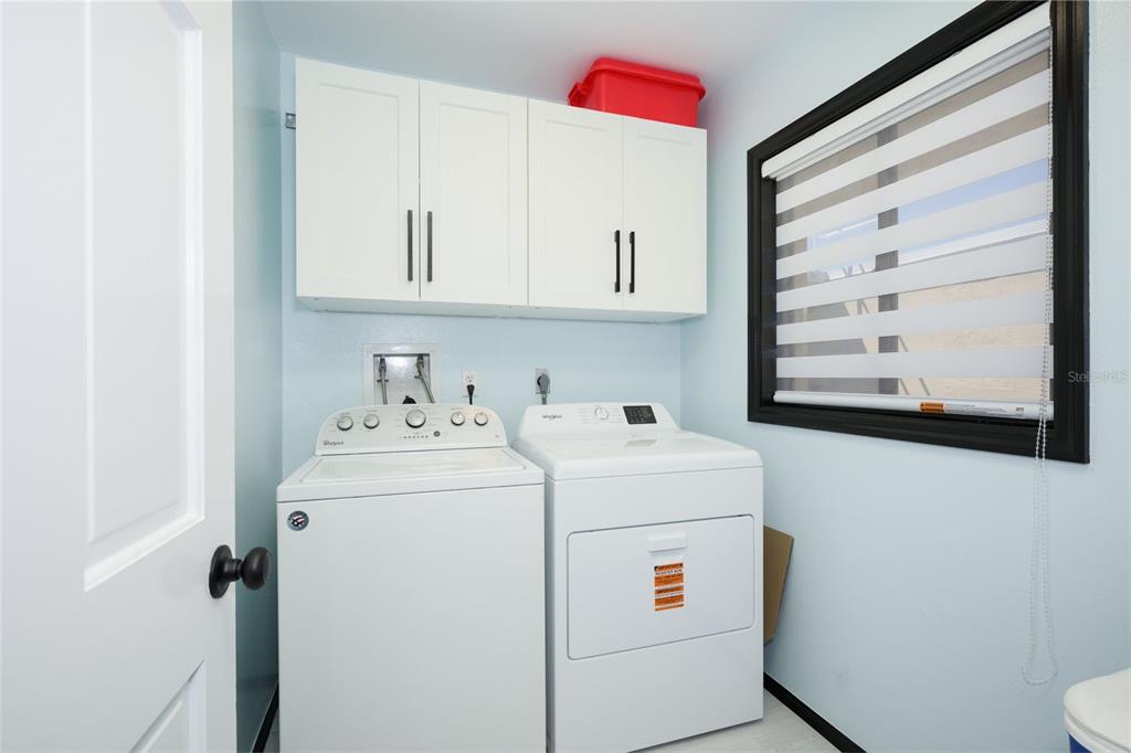A laundry room features a white washer and dryer, upper cabinets, and a window — 2220 OCEAN SHORE BOULEVARD UNIT 505A, ORMOND BEACH, FL