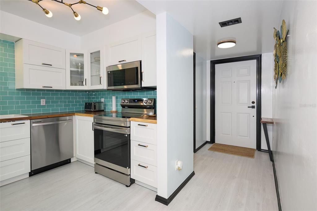 A kitchen with white cabinets, stainless steel appliances, and teal subway tile backsplash — 2220 OCEAN SHORE BOULEVARD UNIT 505A, ORMOND BEACH, FL