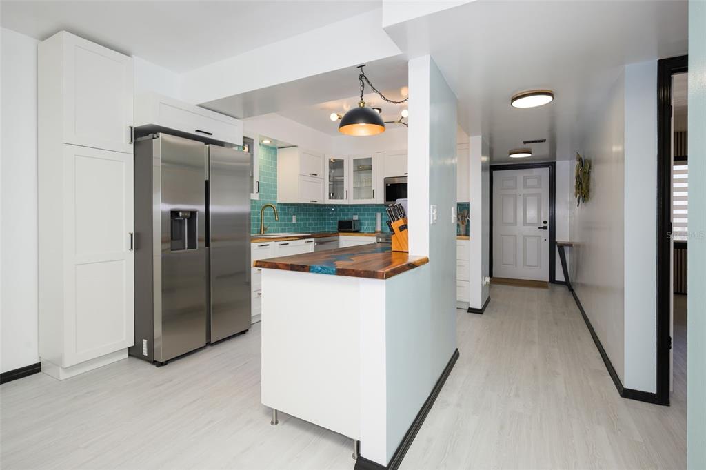 A kitchen features white cabinets, stainless steel appliances, a blue tiled backsplash, and a wood-topped island — 2220 OCEAN SHORE BOULEVARD UNIT 505A, ORMOND BEACH, FL