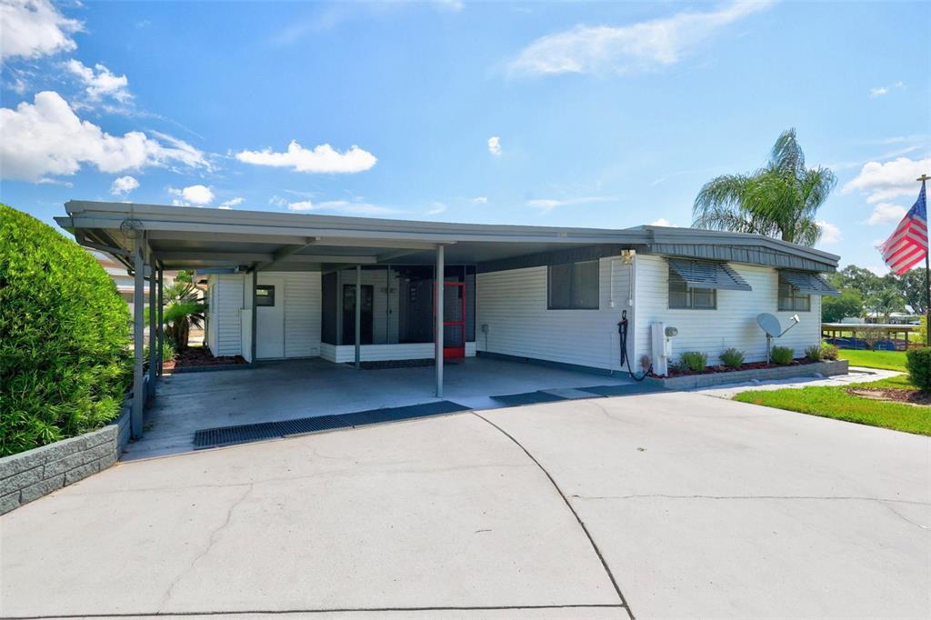 A single-story manufactured home with a carport, concrete driveway, and a small front lawn — 34312 CARL ROAD, LEESBURG, FL