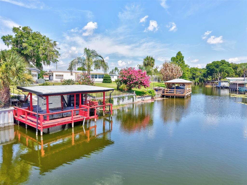 A single-story mobile home with a large carport and a concrete driveway under a blue sky — 34312 CARL ROAD, LEESBURG, FL