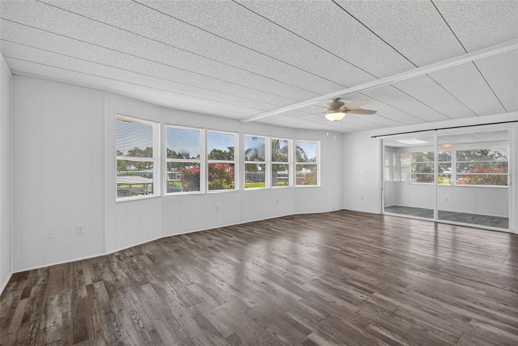 A bright living room features white paneled walls, wood-look flooring, a ceiling fan, and large windows — 34312 CARL ROAD, LEESBURG, FL