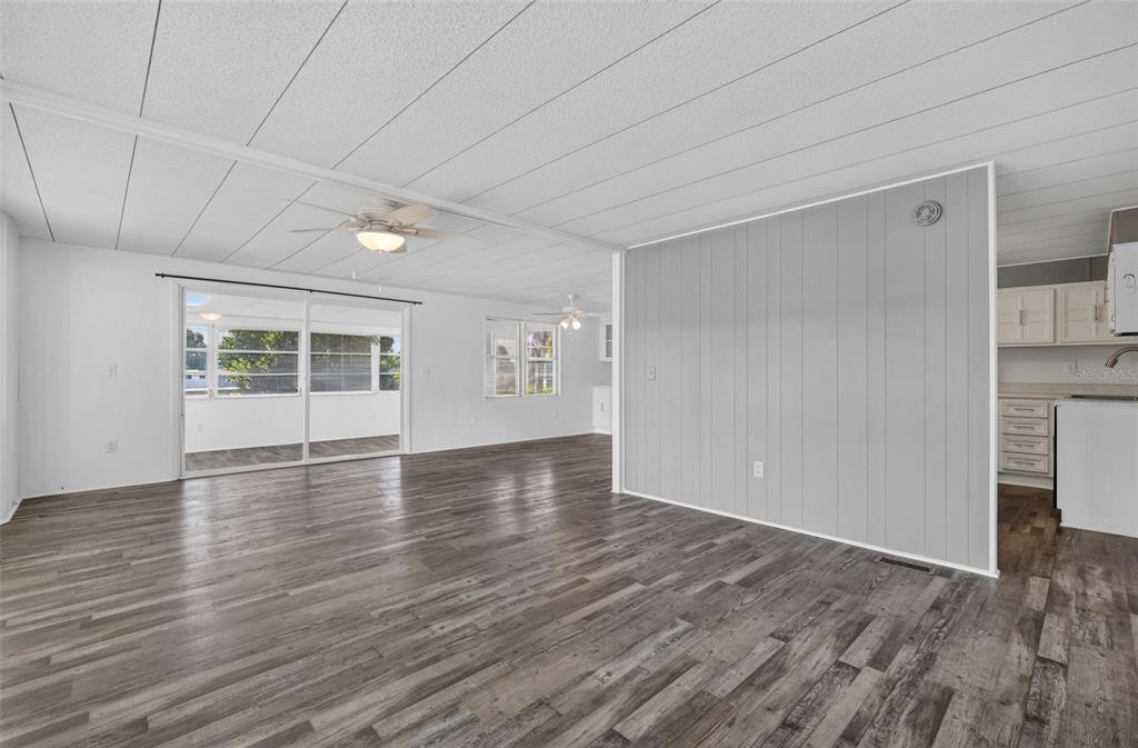 An open-concept living area features gray wood-look flooring, white walls, and a paneled accent wall — 34312 CARL ROAD, LEESBURG, FL