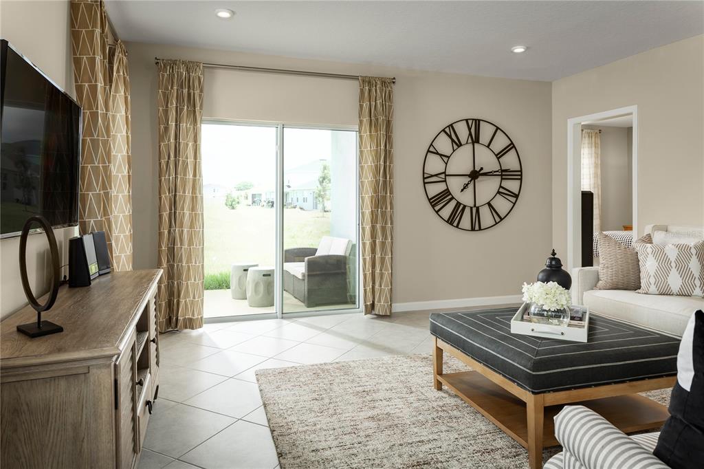 A living room features a large wall clock, sliding glass doors, and a central ottoman — 2228 SCENIC PARK LOOP, WIMAUMA, FL