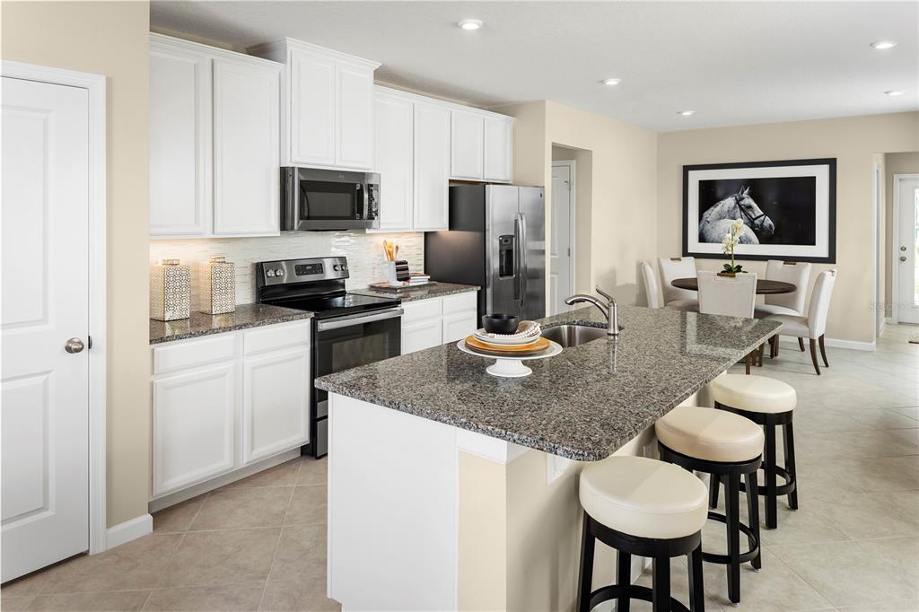 A kitchen with white cabinets, granite countertops, a center island, and an adjacent dining area — 2228 SCENIC PARK LOOP, WIMAUMA, FL