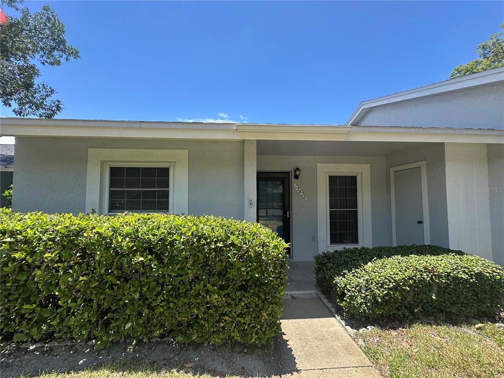 A light-colored house exterior features a front entrance, a walkway, and manicured green hedges — 12423 DEARBORN DRIVE UNIT E, HUDSON, FL