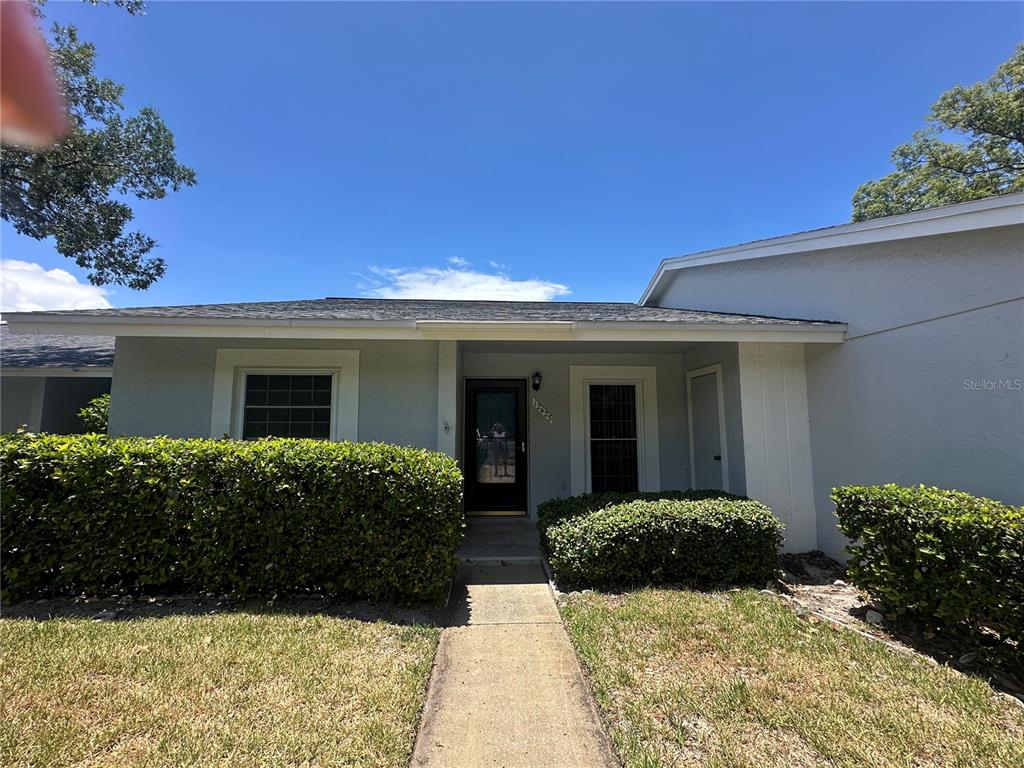 A single-story house exterior features a front walkway, manicured hedges, and a covered entryway — 12423 DEARBORN DRIVE UNIT E, HUDSON, FL