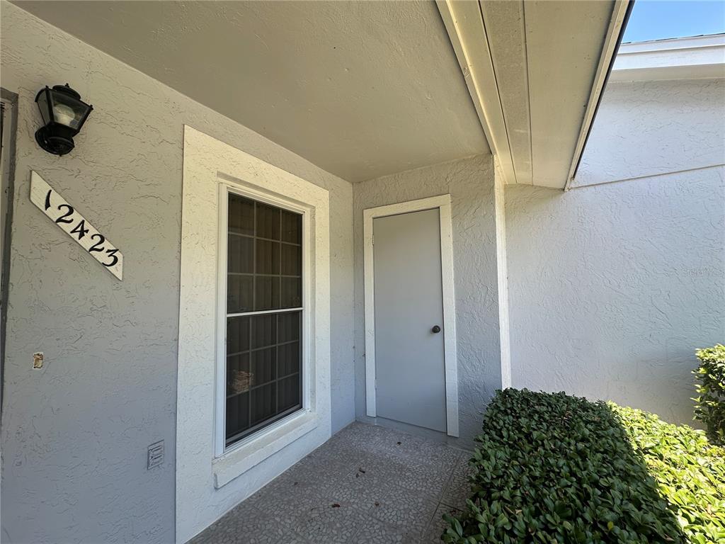 A light gray exterior wall features a window, a door, and a house number plaque — 12423 DEARBORN DRIVE UNIT E, HUDSON, FL