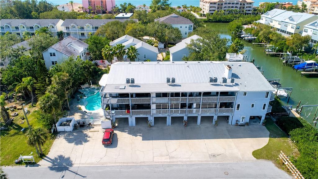 An aerial view shows a multi-story residential building with a pool, parking area, and canal — 512 2ND STREET UNIT 5, INDIAN ROCKS BEACH, FL