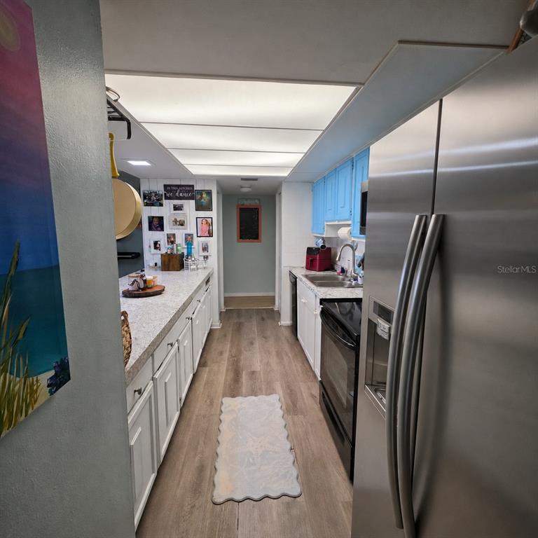 A galley kitchen features white lower cabinets, blue upper cabinets, stainless steel appliances, and wood-look flooring — 512 2ND STREET UNIT 5, INDIAN ROCKS BEACH, FL