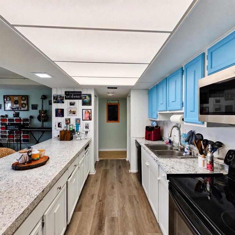 A kitchen features white lower cabinets, bright blue upper cabinets, granite countertops, and wood-look flooring — 512 2ND STREET UNIT 5, INDIAN ROCKS BEACH, FL