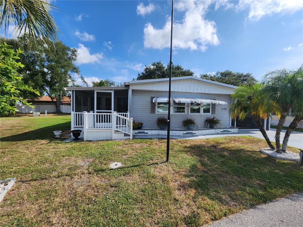A single-story manufactured home with light gray siding, a screened porch, and a palm tree — 808 53RD AVENUE E UNIT 110, BRADENTON, FL