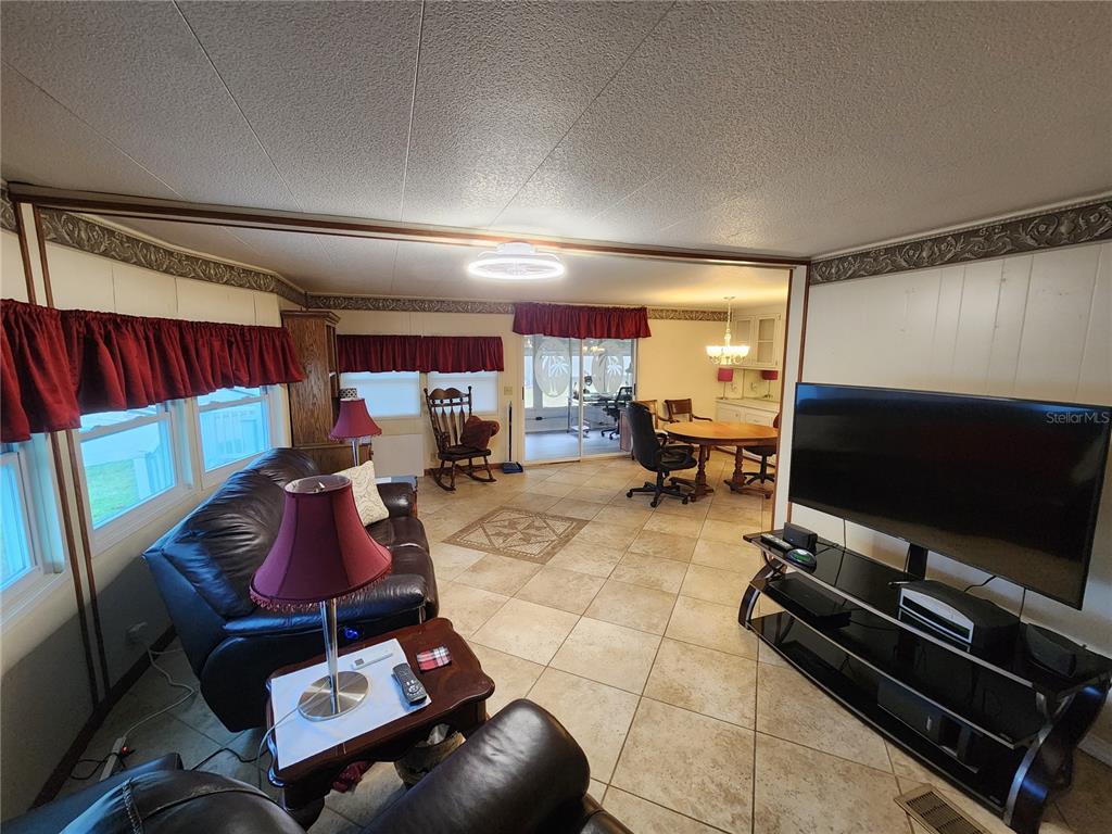 A living room with tile floors, a large television, and a dining area in the background — 808 53RD AVENUE E UNIT 110, BRADENTON, FL