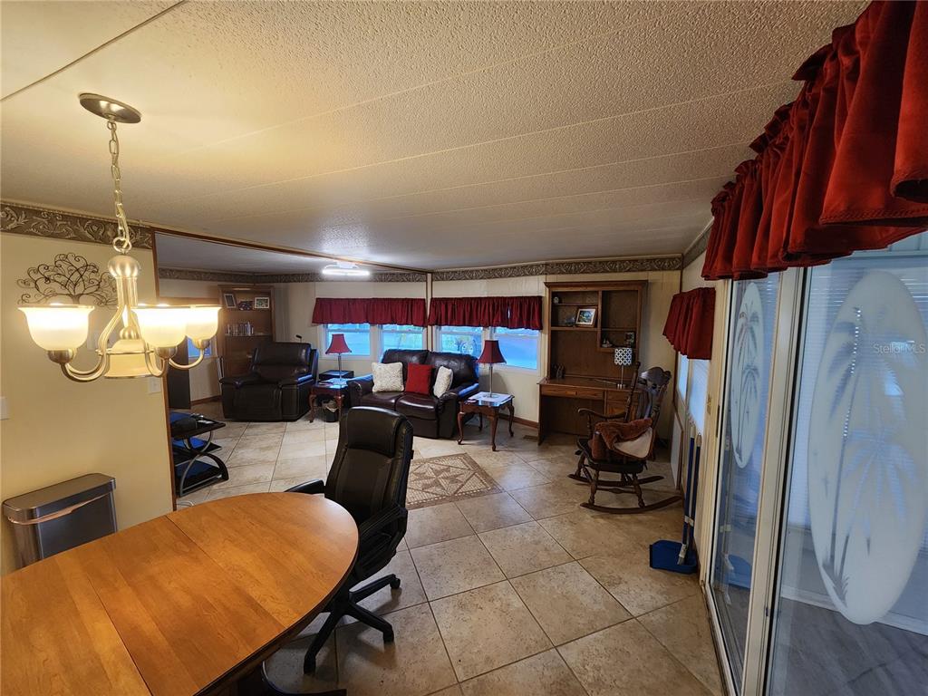 A living and dining area features tile flooring, a chandelier, and a wooden desk — 808 53RD AVENUE E UNIT 110, BRADENTON, FL