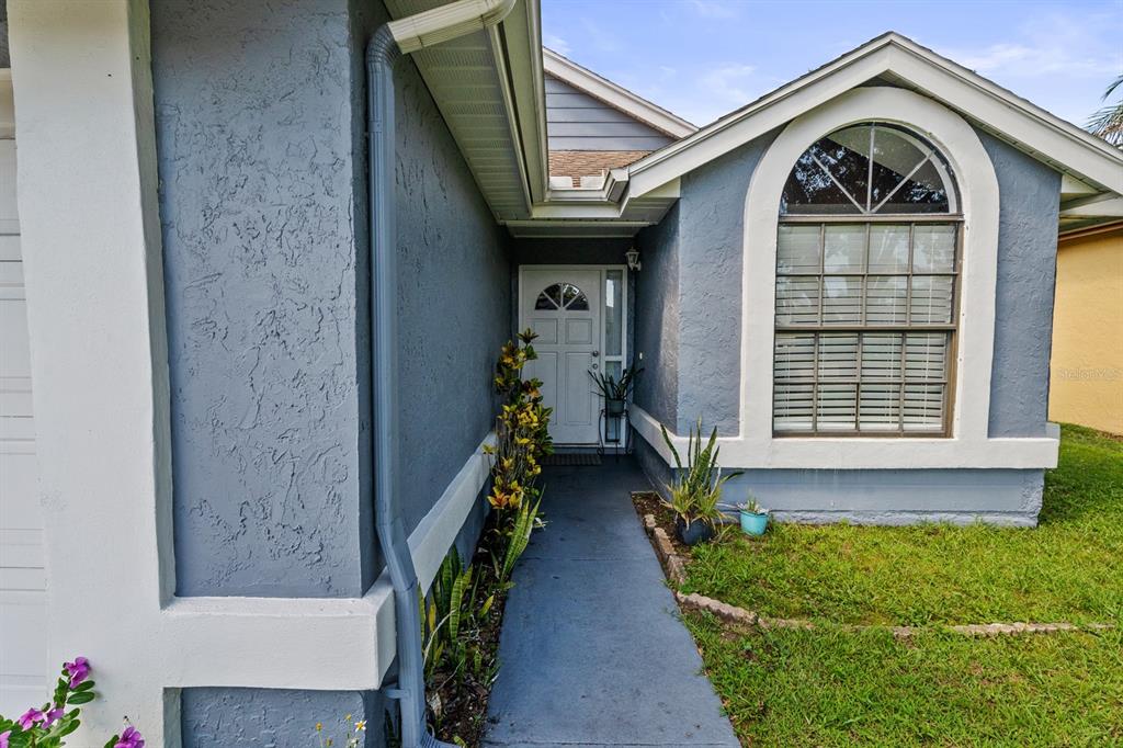 The exterior of a house features a blue stucco facade, a white front door, and a window — 10133 MARGUEX DRIVE, ORLANDO, FL