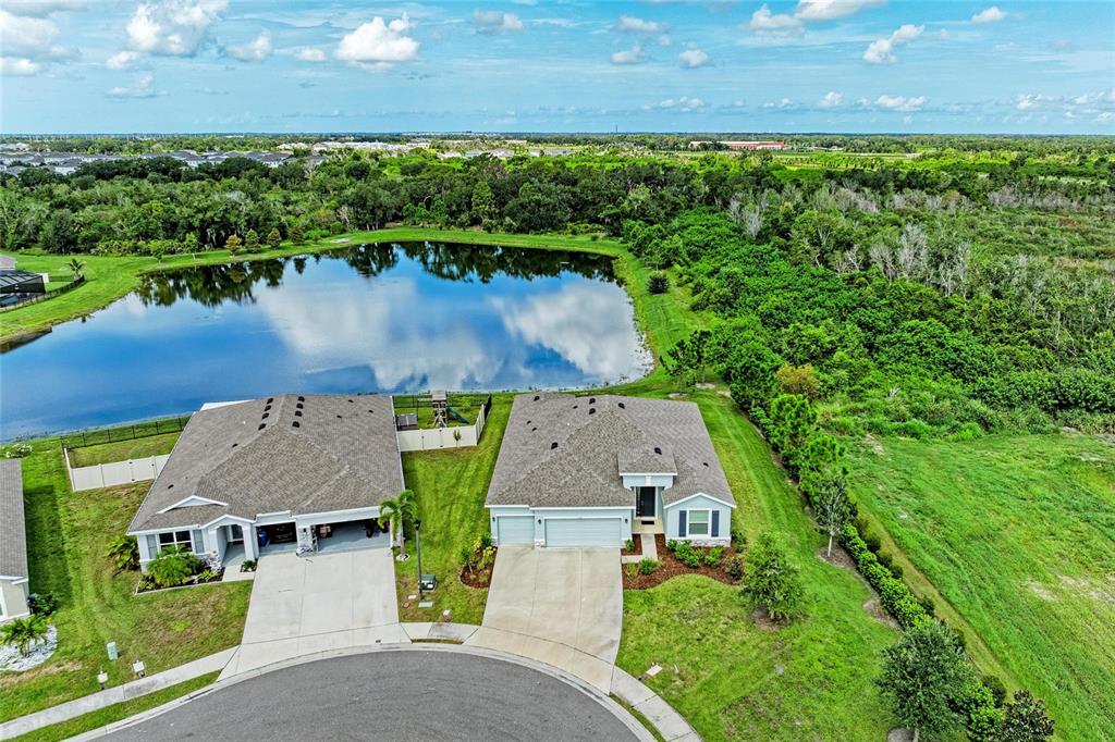An aerial view shows two suburban houses with driveways situated next to a large pond — 11007 TAMARACK PLACE, PARRISH, FL