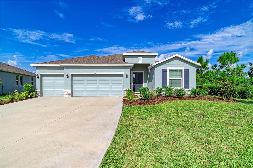 A single-story house with a light-colored stucco exterior, a three-car garage, and a front lawn — 11007 TAMARACK PLACE, PARRISH, FL