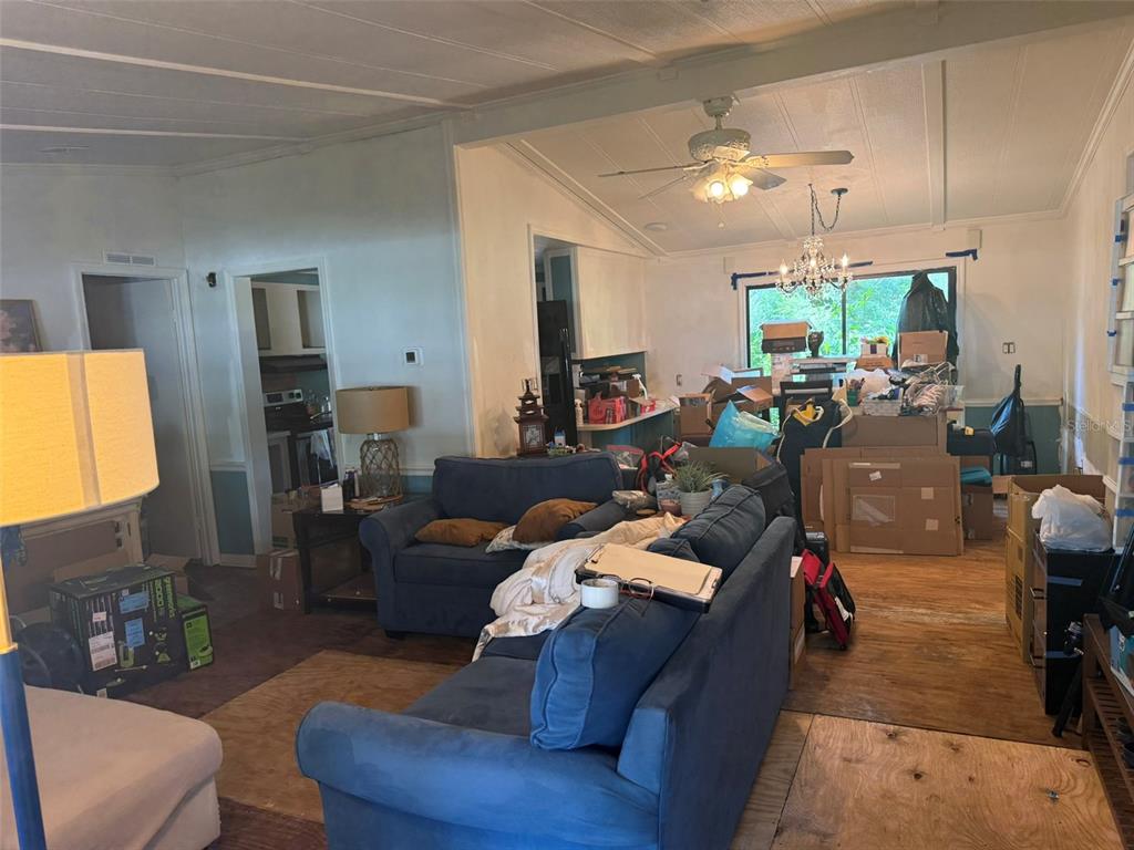 A living room with blue sofas, exposed plywood flooring, and boxes near a dining area — 3210 ROY BURT ROAD, LAKELAND, FL