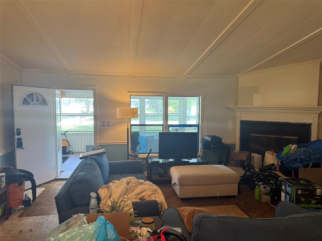 A living room features a fireplace, a blue sofa, a television, and an open front door — 3210 ROY BURT ROAD, LAKELAND, FL