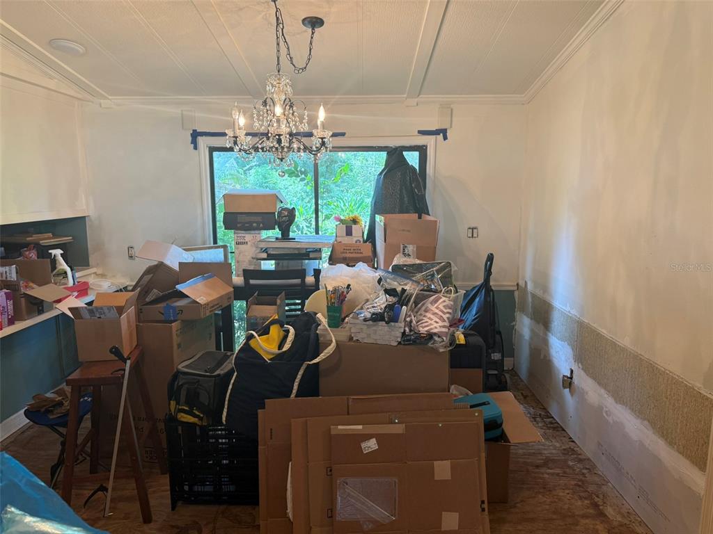 A cluttered dining room features a crystal chandelier, a large window, and unfinished walls — 3210 ROY BURT ROAD, LAKELAND, FL