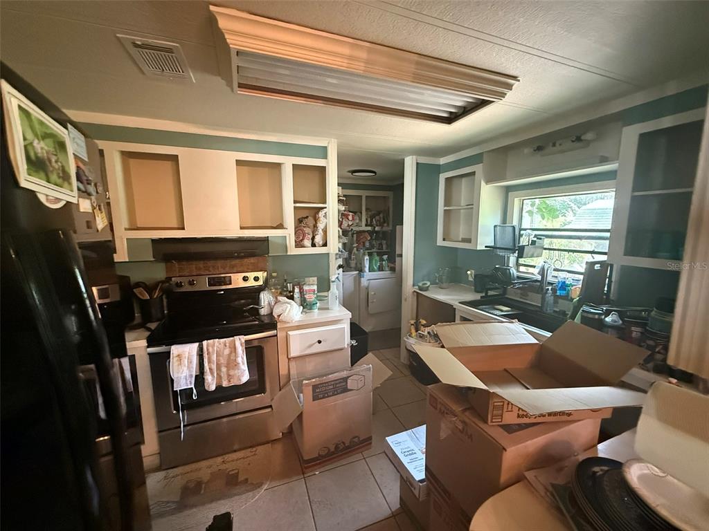 A kitchen with white cabinets, stainless steel appliances, teal walls, and cardboard moving boxes — 3210 ROY BURT ROAD, LAKELAND, FL